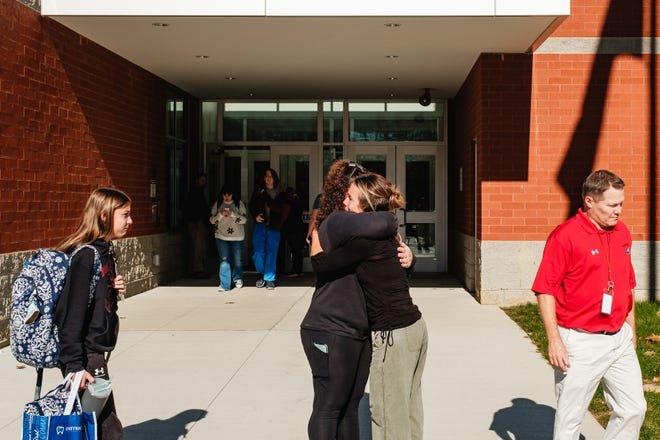 A parent and a teacher embrace outside at Tuscarawas Valley Middle/High School, Tuesday, Nov. 14 in Zoarville, Ohio as children gradually let out of school early.